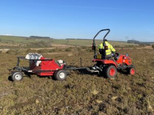 A man in high vis operating a red brush harvester