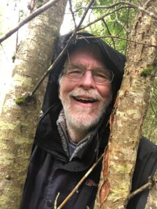 John Box smiling at the camera between two trees.