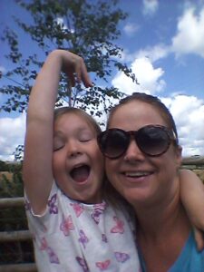 Leila and her daughter. Leila is wearing sunglasses and smiling, her daughter has a big smile on her face with her eyes shut.