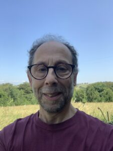 A photo of David Feige CEcol FCIEEM smiling at the camera and wearing a dark purple tshirt 