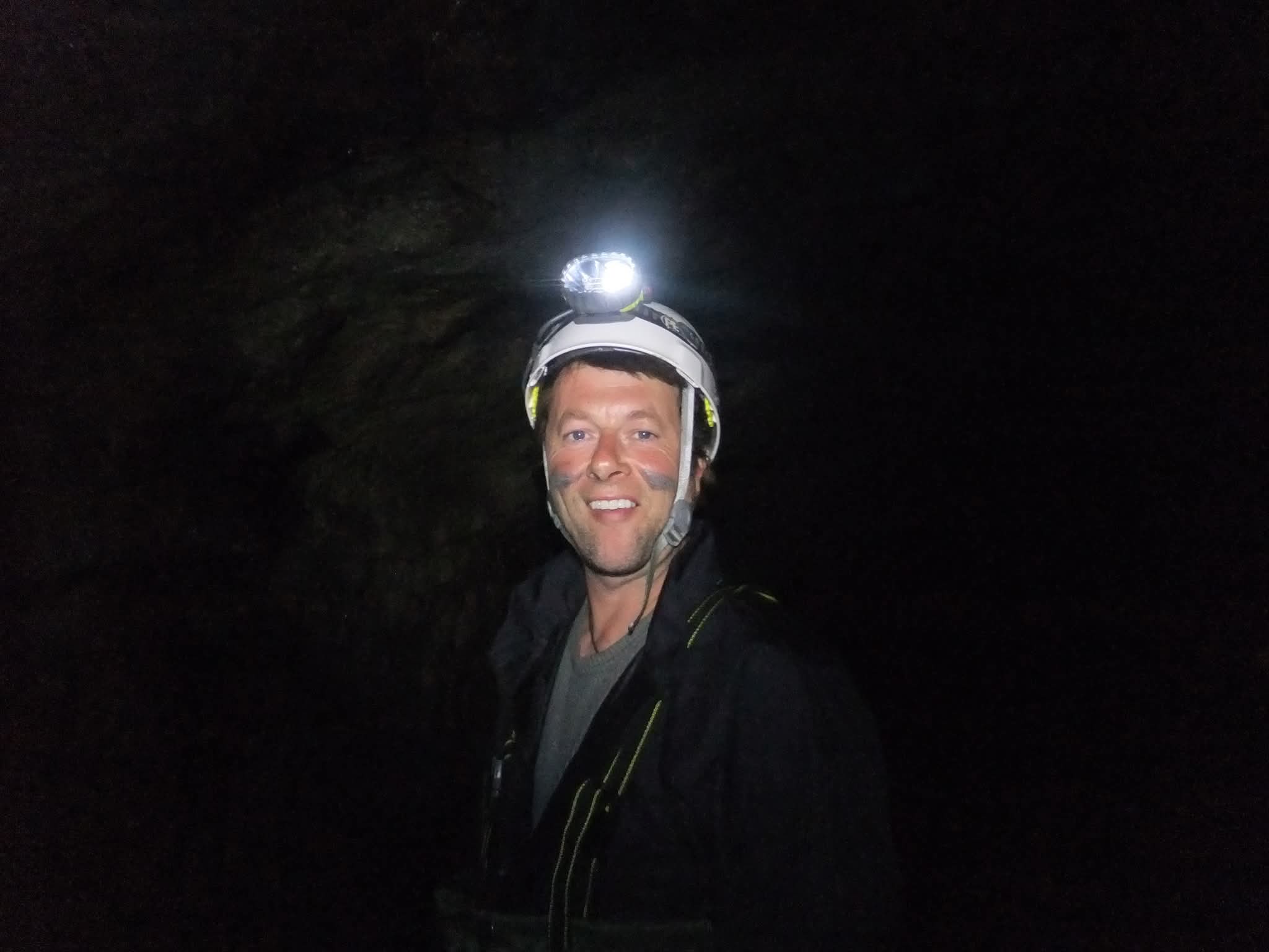 Paul is seen in the dark wearing a helmet and headtorch and smiling broadly.