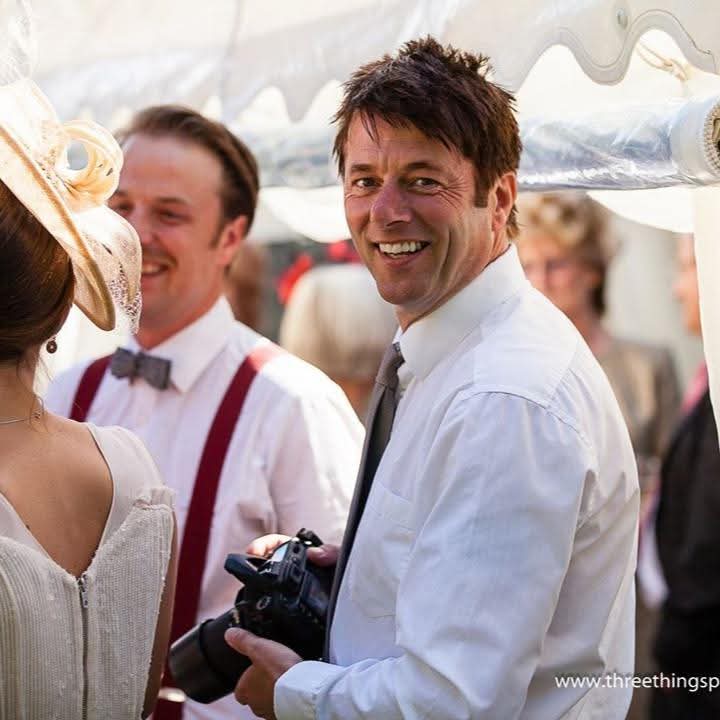 Paul is stood side on to the camera with a broad smile. He is wearing a white shirt and tie and looks to be at a special event.