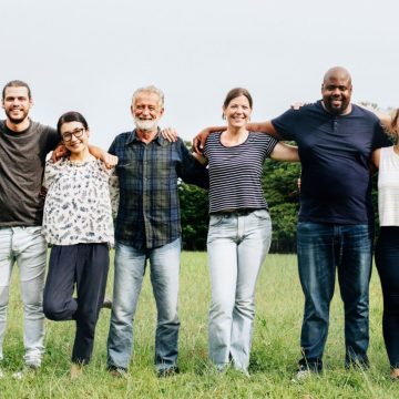 A group of diverse people standing in a field with their arms around each other