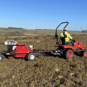 A man in high vis operating a red brush harvester