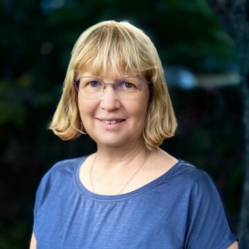 Dr Katie Medcald CEcol FCIEEM smiling at the camera, She has a blonde bob and is wearing glasses and a blue tshirt.