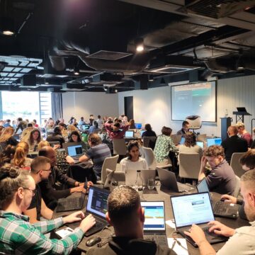 The MKO team at an AI training day - the image shows a room of people sat around circular tables, each with a laptop in front of them