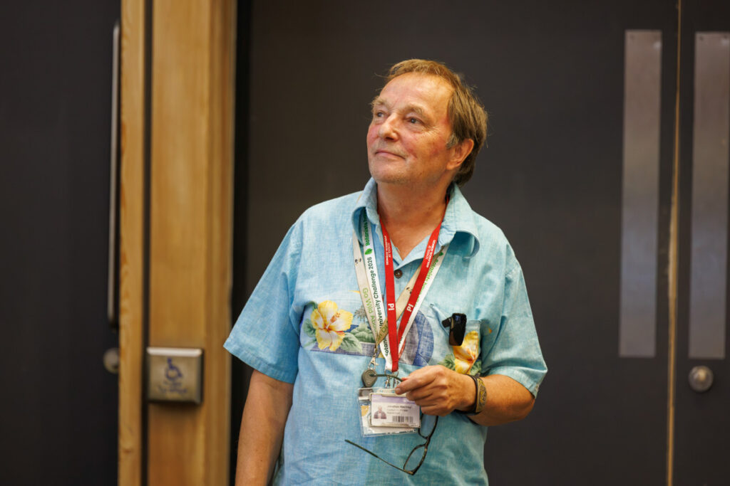 Dr M is wearing a blue shirt and a red lanyard. He has brunette hair and is looking to the side with a calm, happy expression.